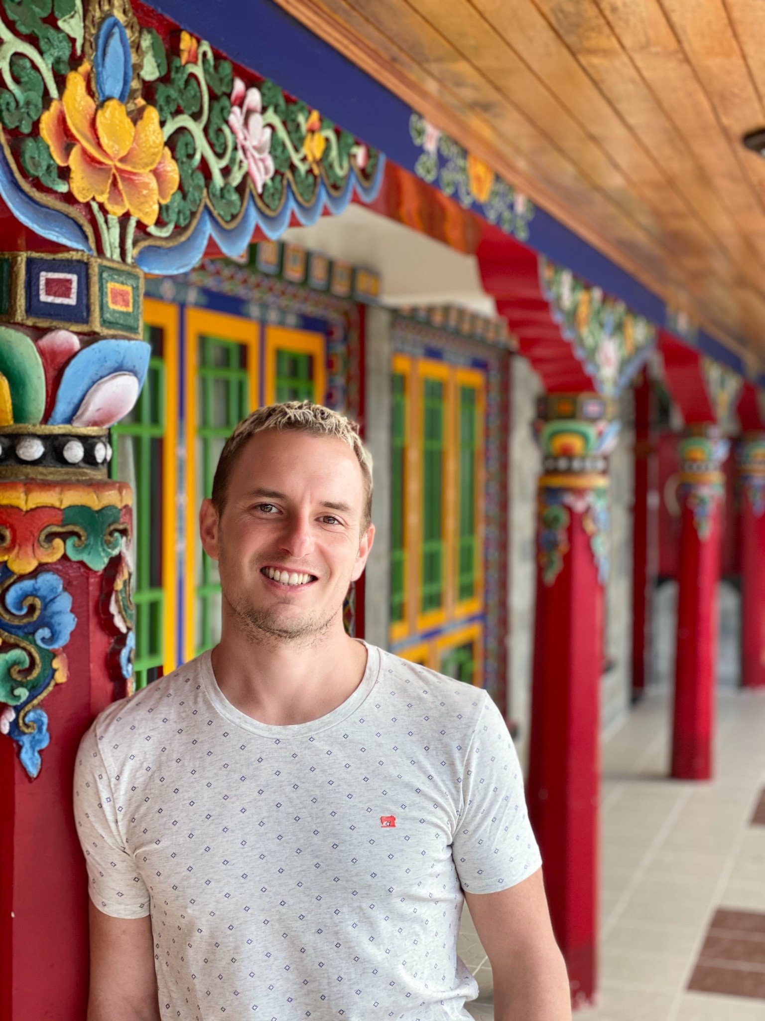 Ty Walrod smiling beside colorful carved architecture